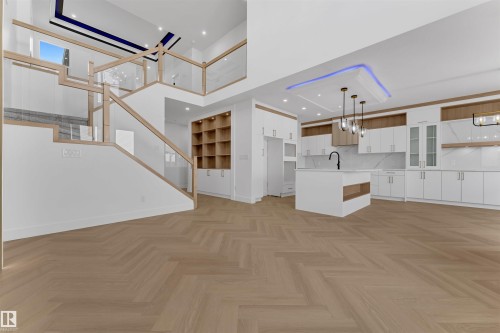 Open-concept interior featuring herringbone wood-finish flooring, a contemporary kitchen with a central island and pendant lighting, a multi-level staircase with glass railings, and built-in shelving - 12 Dalquist Bay, Leduc, AB - Indoor Photo Showing Kitchen