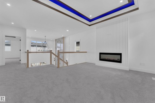 Recessed ceiling with integrated blue lighting, modern linear electric fireplace, white vertical panel accent wall, light grey carpet flooring, and contemporary wood and glass railing - 12 Dalquist Bay, Leduc, AB - Indoor With Fireplace