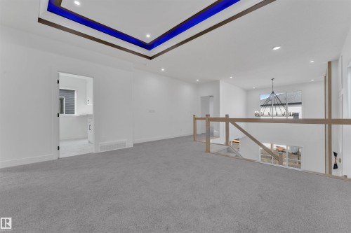 Spacious open-concept landing featuring gray carpet flooring, a contemporary wood-finish and glass railing, and a tray ceiling with recessed lighting - 12 Dalquist Bay, Leduc, AB - Indoor Photo Showing Other Room