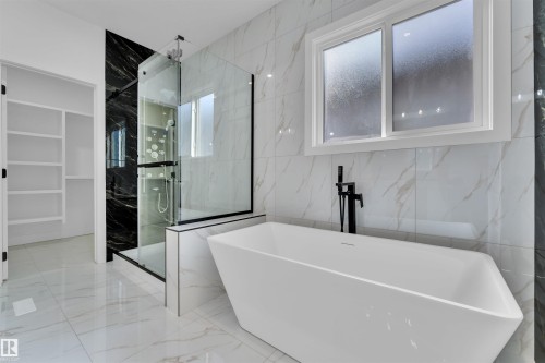 Freestanding soaking tub with a matte black floor-mounted faucet, set against a backdrop of white and grey veined wall tiling - 12 Dalquist Bay, Leduc, AB - Indoor