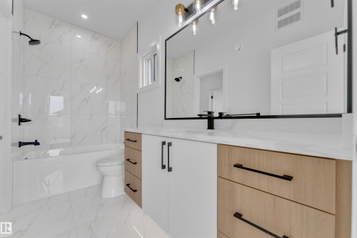 Contemporary bathroom featuring a large vanity with white and wood-finish cabinetry, a white countertop, and a rectangular mirror - 12 Dalquist Bay, Leduc, AB - Indoor Photo Showing Bathroom