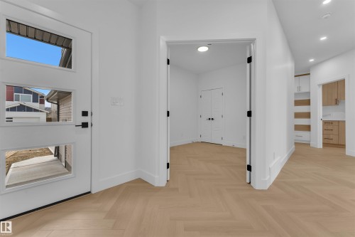 Modern entryway featuring a white paneled door with rectangular glass inserts, black hardware, and wood-finish flooring in a herringbone pattern - 12 Dalquist Bay, Leduc, AB - Indoor Photo Showing Other Room