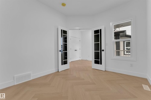 Room featuring wood-finish herringbone flooring, a single pane window, and double French doors with black hardware - 12 Dalquist Bay, Leduc, AB - Indoor Photo Showing Other Room