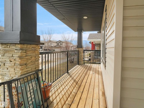 Covered front porch featuring wood-finish flooring, black metal railings, and a stone-clad pillar - 5192 1B Ave Sw, Edmonton, AB - Outdoor With Deck Patio Veranda With Exterior