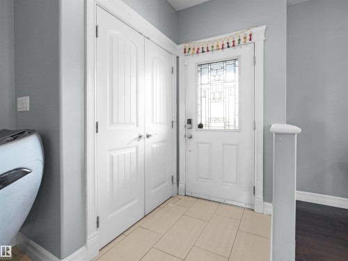 Entryway featuring a white paneled door with decorative glass inserts and a smart lock, light-toned tile flooring, and a double closet with white paneled bifold doors - 5192 1B Ave Sw, Edmonton, AB - Indoor Photo Showing Other Room