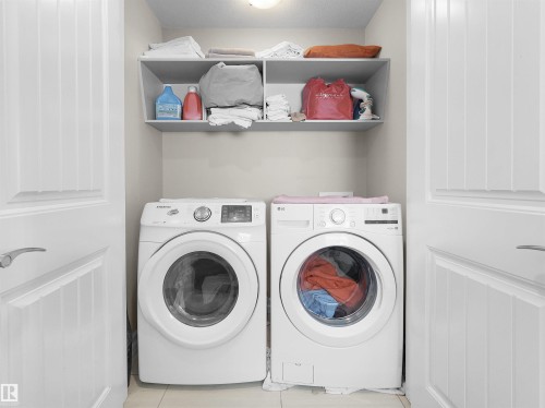 Dedicated laundry space featuring a front-loading washer and dryer, overhead shelving, and tiled flooring - 5192 1B Ave Sw, Edmonton, AB - Indoor Photo Showing Laundry Room