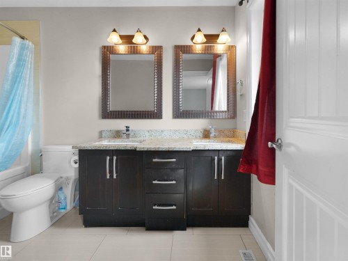 Dual vanity featuring stone-finish countertop, undermount sinks, and dark wood-finish cabinetry - 5192 1B Ave Sw, Edmonton, AB - Indoor Photo Showing Bathroom