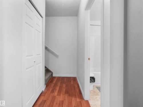 Hallway featuring wood-finish flooring, a bi-fold closet, and a carpeted staircase with a white handrail - 5192 1B Ave Sw, Edmonton, AB - Indoor