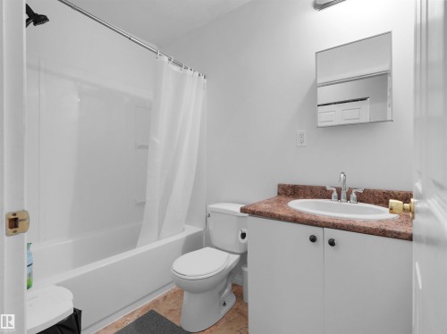 Full bathroom featuring a white porcelain toilet, white vanity with a brown-toned countertop, oval undermount sink, and a combination bathtub/shower with a black showerhead - 5192 1B Ave Sw, Edmonton, AB - Indoor Photo Showing Bathroom