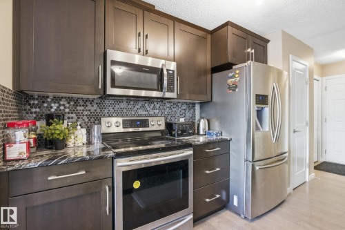 Kitchen featuring dark wood-finish cabinetry, stainless steel appliances, a mosaic tile backsplash, and a patterned countertop - 893 Ebbers Crescent Nw, Edmonton, AB - Indoor Photo Showing Kitchen
