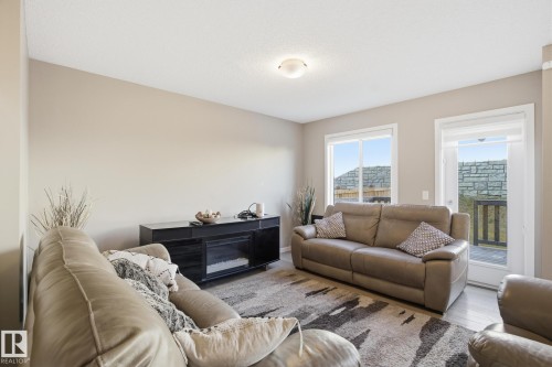 Living area featuring light neutral wall paint, a built-in electric fireplace unit with a dark finish, wood-finish flooring, a ceiling-mounted light fixture, and large windows - 893 Ebbers Crescent Nw, Edmonton, AB - Indoor Photo Showing Living Room