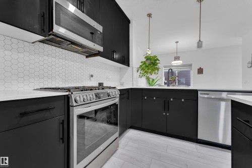 Modern kitchen featuring stainless steel appliances, black cabinetry, white countertops, a hexagonal tile backsplash, and light wood-finish flooring - 1645 Plum Circle Circle, Edmonton, AB - Indoor Photo Showing Kitchen With Upgraded Kitchen