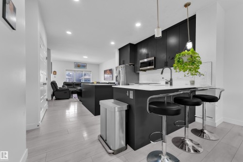 Contemporary kitchen featuring dark cabinetry, stainless steel appliances, a white tile backsplash, a kitchen island with seating, and wood-finish flooring - 1645 Plum Circle Circle, Edmonton, AB - Indoor Photo Showing Kitchen With Upgraded Kitchen
