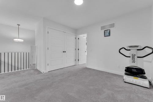 Carpeted landing area featuring a modern pendant light, white paneled doors, and a staircase with a black metal railing - 1645 Plum Circle Circle, Edmonton, AB - Indoor Photo Showing Other Room