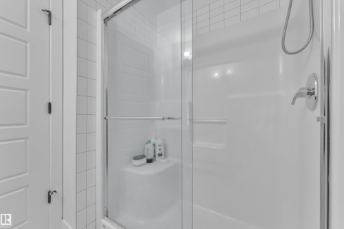 Shower enclosure featuring a frameless glass door, white subway tile surround, integrated shelving, and a chrome showerhead with a handheld spray - 1645 Plum Circle Circle, Edmonton, AB - Indoor Photo Showing Bathroom
