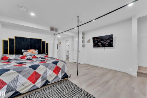 Spacious bedroom featuring wood-finish flooring, recessed lighting, a built-in wall-mounted television, and a track lighting system - 1645 Plum Circle Circle, Edmonton, AB - Indoor Photo Showing Bedroom