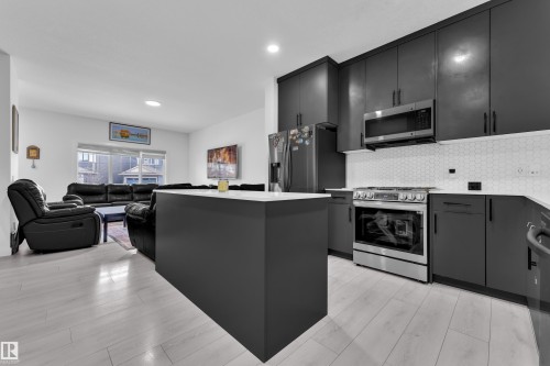 Modern kitchen featuring dark cabinetry, stainless steel appliances, a white hexagon tile backsplash, and light wood-finish flooring - 1645 Plum Circle Circle, Edmonton, AB - Indoor Photo Showing Kitchen