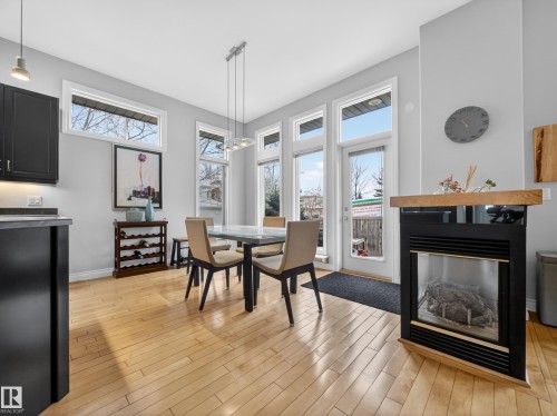 Dining area featuring light wood-finish flooring, a contemporary fireplace with a wood mantle, and multiple large windows - 569 Butterworth Way, Edmonton, AB - Indoor Photo Showing Dining Room With Fireplace