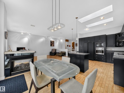Open-concept living space with light wood-finish flooring, a built-in fireplace featuring a stone-look mantel, and a kitchen area - 569 Butterworth Way, Edmonton, AB - Indoor