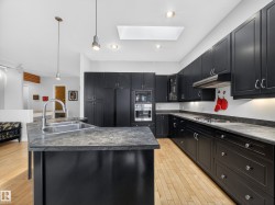 Modern kitchen featuring extensive dark cabinetry, light wood-finish flooring, recessed lighting, a skylight, and a built-in stainless steel oven and microwave - 