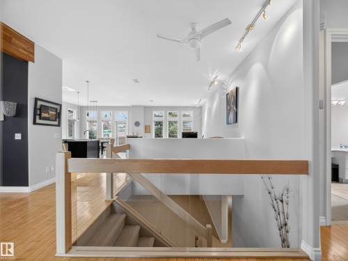 Upper-level landing featuring wood-finish flooring, a modern glass and wood banister, a ceiling fan, and track lighting - 569 Butterworth Way, Edmonton, AB - Indoor Photo Showing Other Room