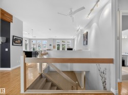 Upper-level landing featuring wood-finish flooring, a modern glass and wood banister, a ceiling fan, and track lighting - 