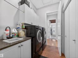 Dedicated laundry area featuring modern appliances, a utility sink with a high-arch faucet, granite-look countertop, and white shaker-style cabinetry - 