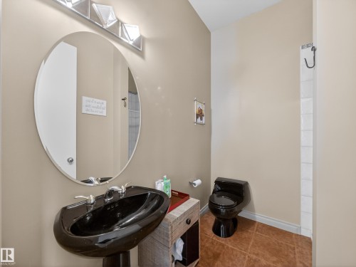 Bathroom featuring a black pedestal sink, an oval wall-mounted mirror, and a black toilet - 569 Butterworth Way, Edmonton, AB - Indoor