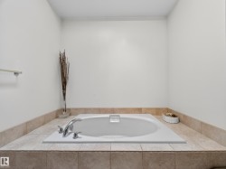 White drop-in tub with chrome fixtures, set within a tiled surround featuring neutral-toned ceramic tiles - 