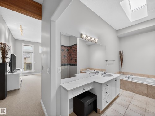 Bathroom featuring a double vanity with integrated sinks, a built-in bathtub, tile flooring, a skylight, and an adjacent dressing area - 569 Butterworth Way, Edmonton, AB - Indoor