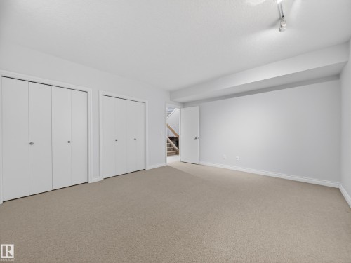 Spacious room featuring neutral carpet flooring, two sets of white bi-fold closet doors, and white painted walls - 569 Butterworth Way, Edmonton, AB - Indoor Photo Showing Other Room