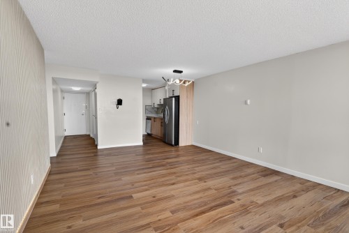Spacious living area featuring wood-finish flooring, a contemporary ceiling fixture, and a kitchen area with stainless steel appliances and light wood cabinetry - 90 8745 165 Street, Edmonton, AB - Indoor Photo Showing Other Room