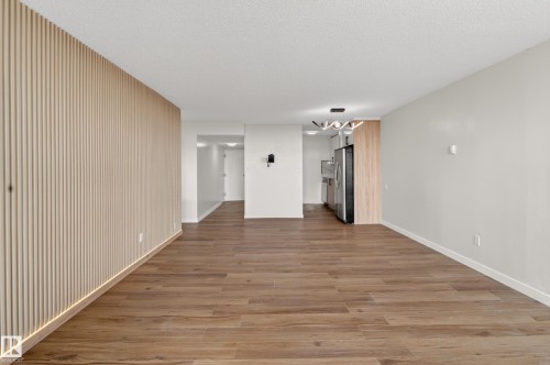Open-concept living area with wood-finish flooring, a contemporary slatted accent wall with integrated strip lighting, and a modern chandelier - 90 8745 165 Street, Edmonton, AB - Indoor Photo Showing Other Room