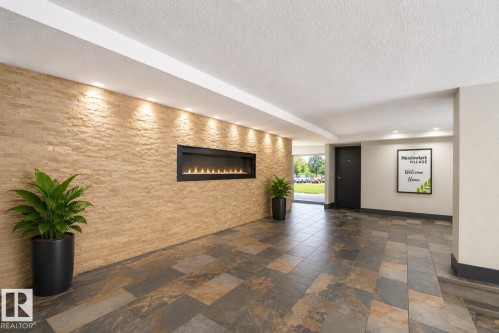 Entryway featuring a stacked stone accent wall with integrated linear fireplace, recessed lighting, and multi-tone slate-style floor tiles - 90 8745 165 Street, Edmonton, AB - Indoor With Fireplace
