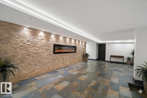 Foyer featuring a stone-clad accent wall with an inset linear electric fireplace, stone tile flooring, recessed ceiling lighting, and crown molding with integrated lighting - 90 8745 165 Street, Edmonton, AB - Indoor Photo Showing Other Room With Fireplace