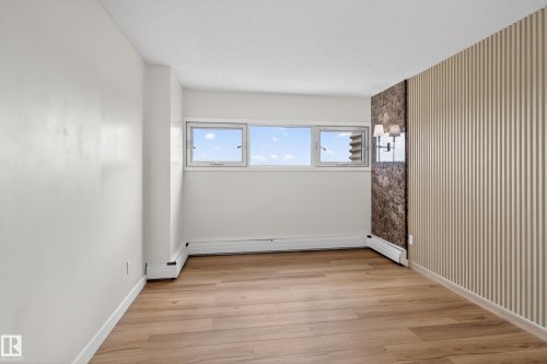 Bright interior space featuring light wood-finish flooring, white painted walls, and textured accent wall panels - 90 8745 165 Street, Edmonton, AB - Indoor Photo Showing Other Room