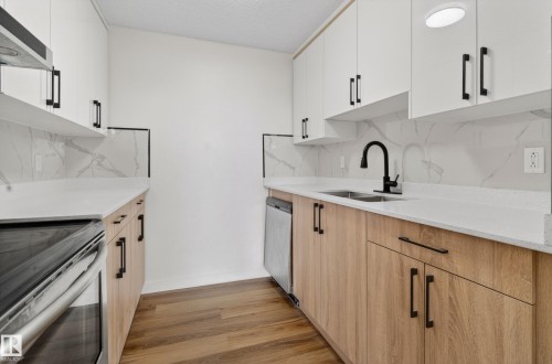Renovated kitchen featuring wood-finish lower cabinetry, white upper cabinetry, and matte black hardware - 90 8745 165 Street, Edmonton, AB - Indoor Photo Showing Kitchen With Double Sink