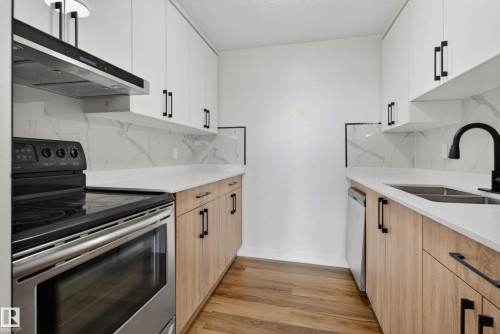 Galley kitchen featuring wood-finish flooring, white upper cabinetry, and light wood-finish lower cabinetry with black hardware - 90 8745 165 Street, Edmonton, AB - Indoor Photo Showing Kitchen With Double Sink