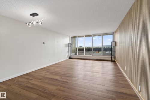 Spacious room with wood-finish flooring, a full wall of floor-to-ceiling windows, and a modern ceiling light fixture - 90 8745 165 Street, Edmonton, AB - Indoor Photo Showing Other Room