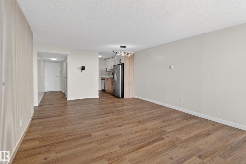 Open-concept living space with wood-finish flooring, light-colored walls, and a textured accent wall - 90 8745 165 Street, Edmonton, AB - Indoor Photo Showing Other Room