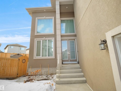 Contemporary stucco exterior with a tall entryway, featuring a double glass panel door and upper transom window - 1208 25 St Nw, Edmonton, AB - Outdoor