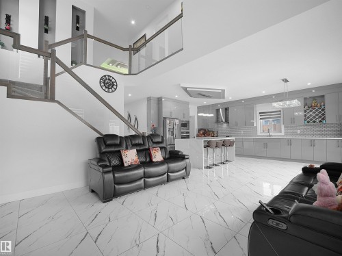 Open-concept living space featuring a contemporary kitchen with gray cabinetry, a central island with bar seating, and white tile flooring - 1208 25 St Nw, Edmonton, AB - Indoor