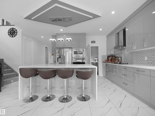 Modern kitchen featuring a large island with seating, glossy gray cabinetry, white subway tile backsplash, and integrated stainless steel appliances - 1208 25 St Nw, Edmonton, AB - Indoor Photo Showing Kitchen With Upgraded Kitchen