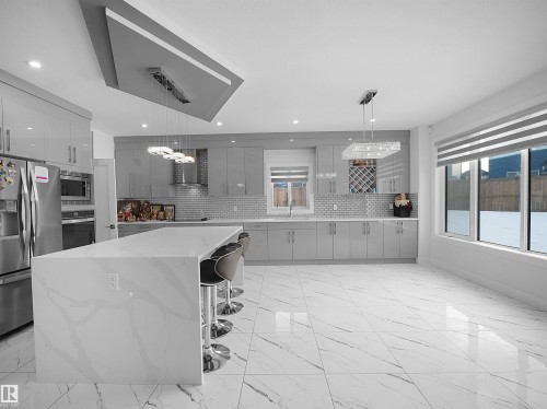 Spacious kitchen featuring an oversized island with a waterfall countertop, sleek gray cabinetry, stainless steel appliances, a subway tile backsplash, and large format marble-look floor tiling - 1208 25 St Nw, Edmonton, AB - Indoor Photo Showing Kitchen With Upgraded Kitchen