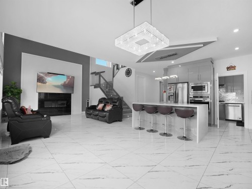 Open-concept living space featuring large format marble-look tile flooring, a contemporary fireplace with a dark surround, and a kitchen island with seating - 1208 25 St Nw, Edmonton, AB - Indoor