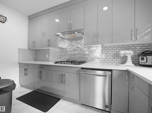 Contemporary kitchen featuring light gray high-gloss cabinetry, white countertop surfaces, a subway tile backsplash, stainless steel dishwasher, and a built-in range hood - 1208 25 St Nw, Edmonton, AB - Indoor Photo Showing Kitchen With Upgraded Kitchen