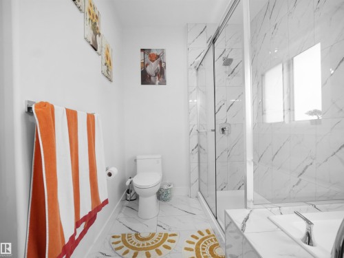 Bathroom featuring white marble-look tile flooring and shower surround, a frameless glass shower enclosure, a built-in bathtub with integrated faucet, and a toilet - 1208 25 St Nw, Edmonton, AB - Indoor Photo Showing Bathroom