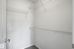 Walk-in closet featuring white wire shelving on two walls, white painted walls, and dark gray carpet flooring - 