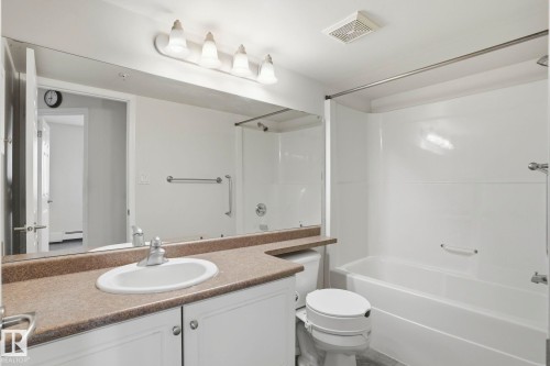 Bathroom featuring a white vanity with a tan speckled countertop, an oval undermount sink, a large wall-mounted mirror, and a white bathtub with a shower enclosure - 120 13625 34 Street, Edmonton, AB - Indoor Photo Showing Bathroom