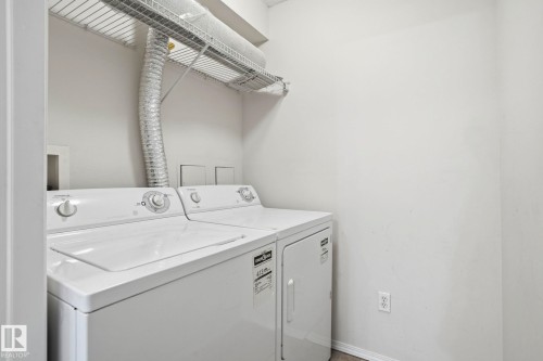 Dedicated laundry area featuring a white top-load washer and dryer set, overhead wire shelving, and neutral wall finishes - 120 13625 34 Street, Edmonton, AB - Indoor Photo Showing Laundry Room